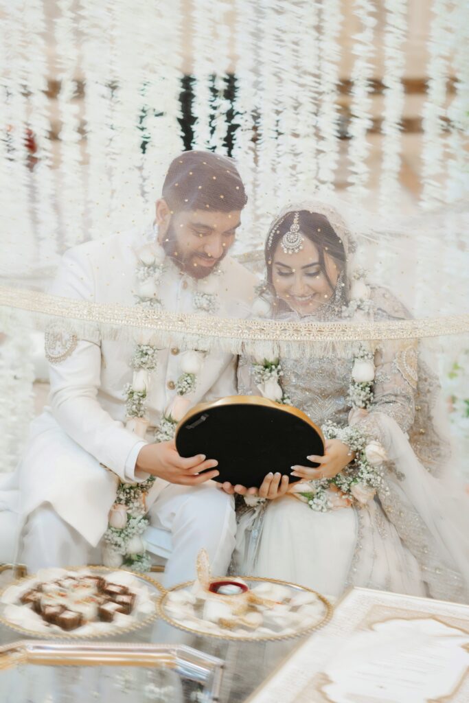 Couple under a shared dupatta looking into a mirror during the aarsi mushaf mirror ceremony at their nikah
