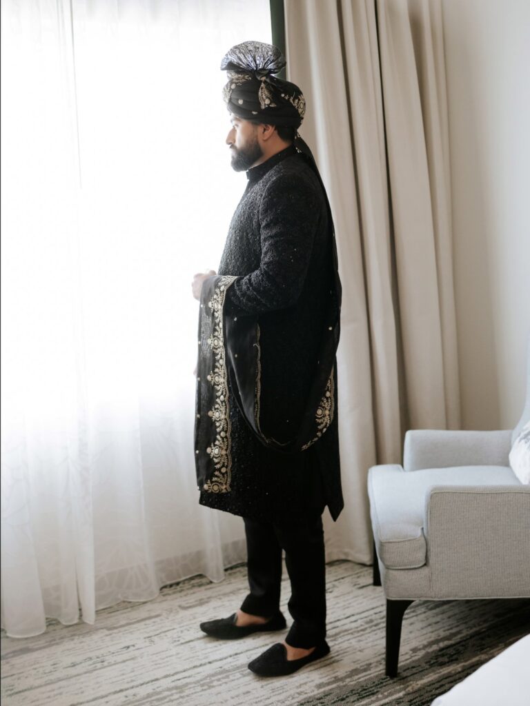 Amen & Shoaib’s Stunning South Asian Wedding at Signia by Hilton & Waldorf Astoria Orlando 15 Groom in a black sherwani and turban standing at the window before his shaadi at a Bonnet Creek resort in Orlando