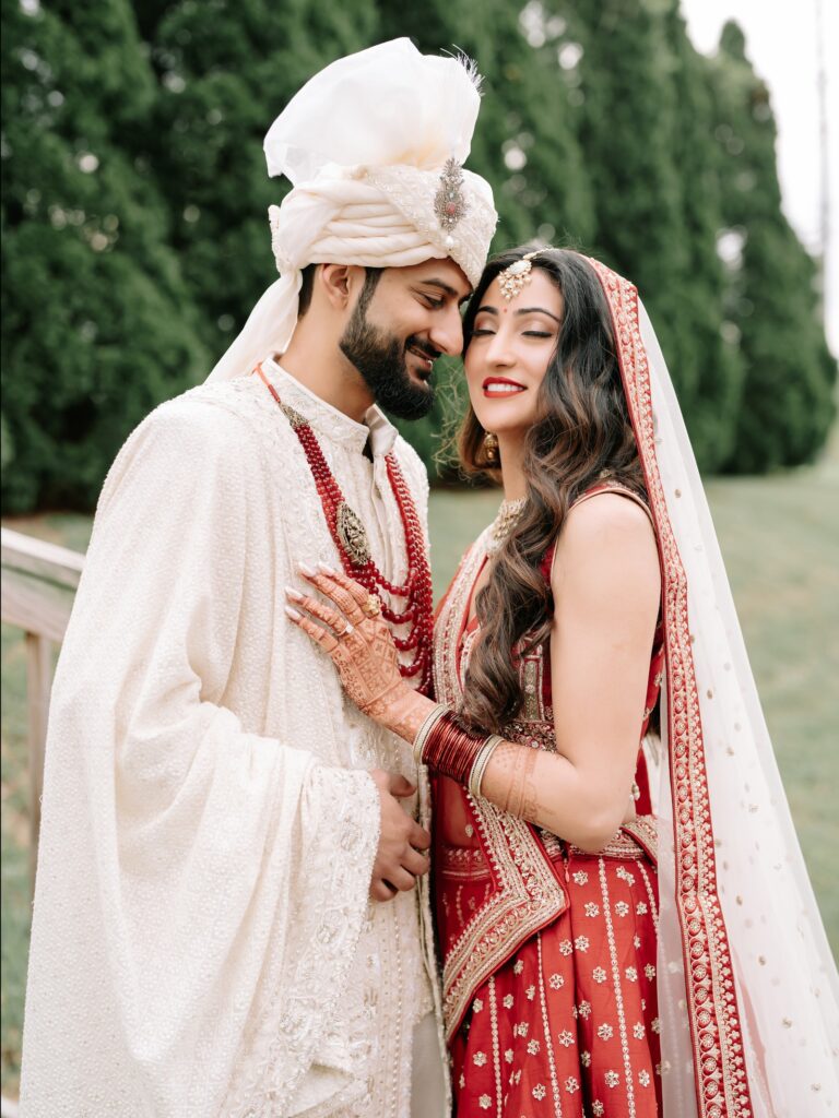 Priya & Dillan’s Gujarati Wedding | Indian Wedding Photographer Atlanta 15 Groom in ivory gently holding the bride in a red lehenga in front of evergreen trees
