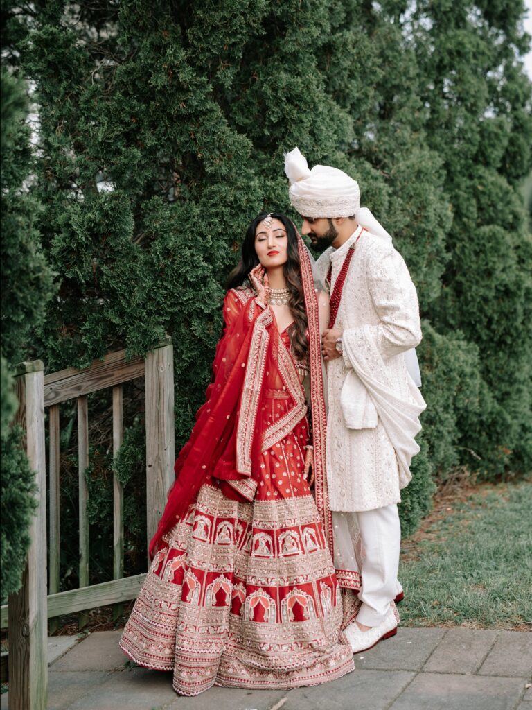 Priya & Dillan’s Gujarati Wedding | Indian Wedding Photographer Atlanta 14 Bride in a red lehenga and groom in ivory standing together in front of evergreens, Hindu wedding portraits
