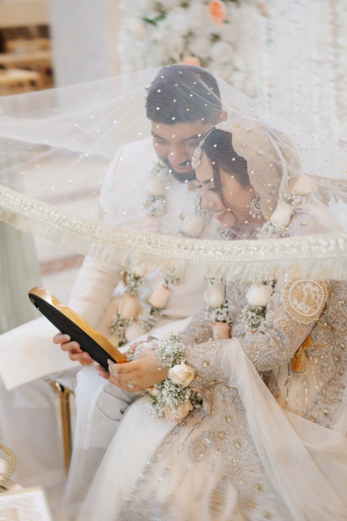 Bride and groom laughing under a sequined dupatta during the mirror ceremony, Muslim wedding photography in Central Florida