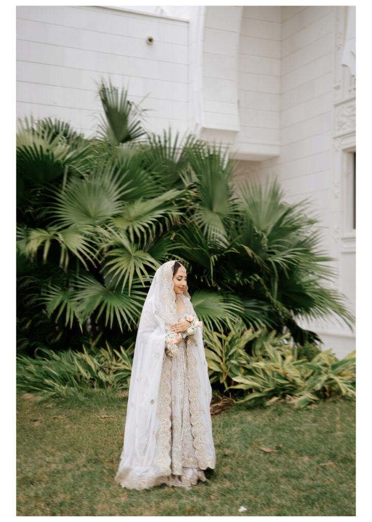 Muslim bride in an ivory and silver embroidered lehenga and dupatta beside palm trees at Masjid Al-Hayy in Sanford, Florida