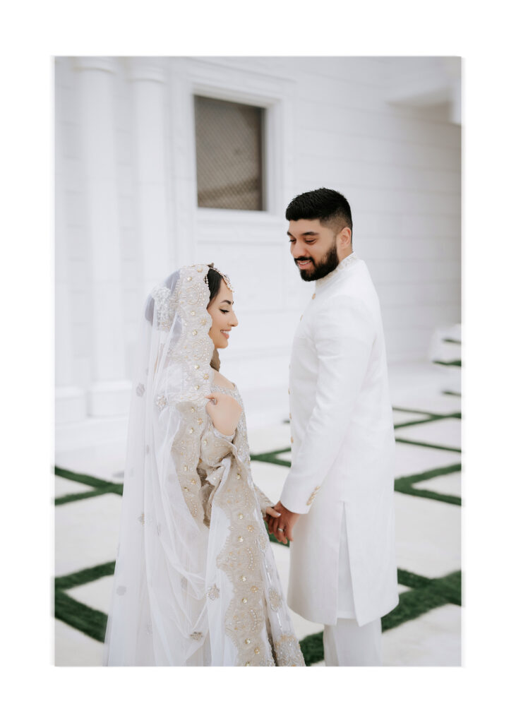 Bride and groom in white holding hands outside the white walls of Masjid Al-Hayy, nikah ceremony in Sanford, Florida