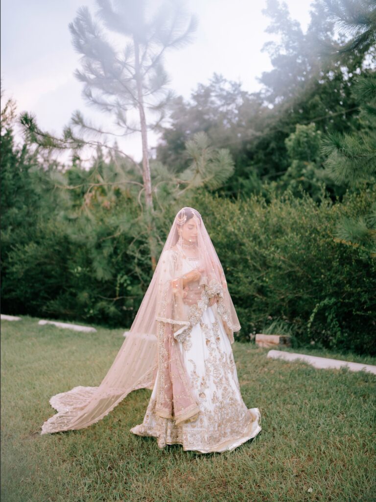 Amen & Shoaib’s Stunning South Asian Wedding at Signia by Hilton & Waldorf Astoria Orlando 11 Bride walking across the lawn in a blush lehenga with a long dupatta among the pines at Bonnet Creek, Orlando