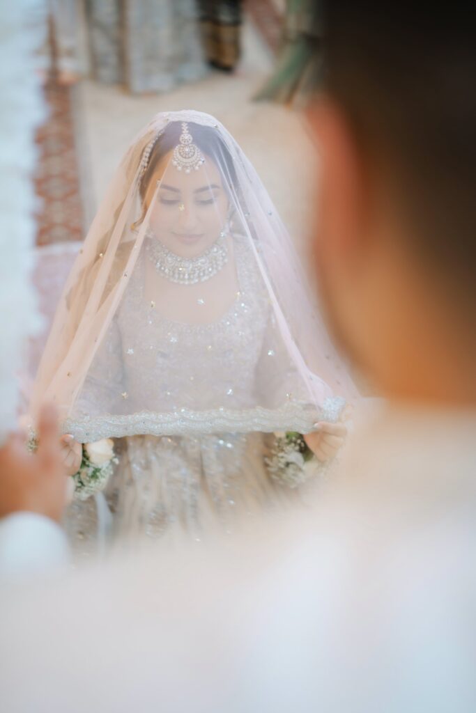 Bride lifting her sheer embellished dupatta during her nikah, seen over the groom’s shoulder