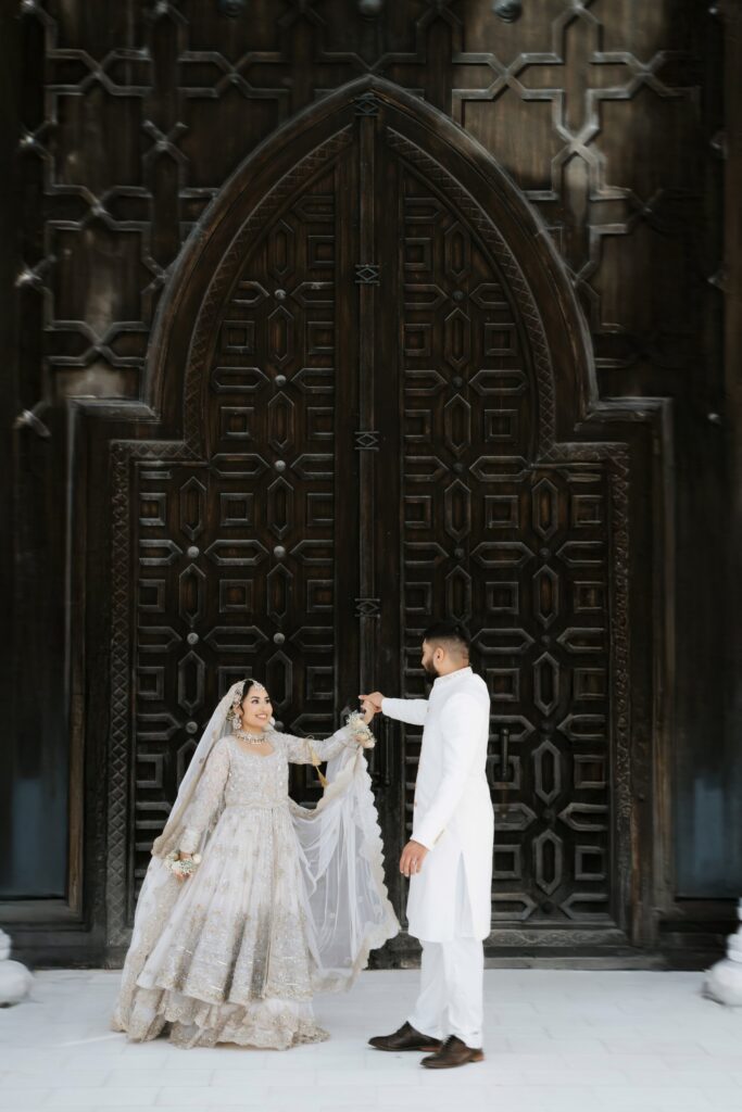 Groom twirling his bride in front of the carved wooden doors of Masjid Al-Hayy on their nikah day