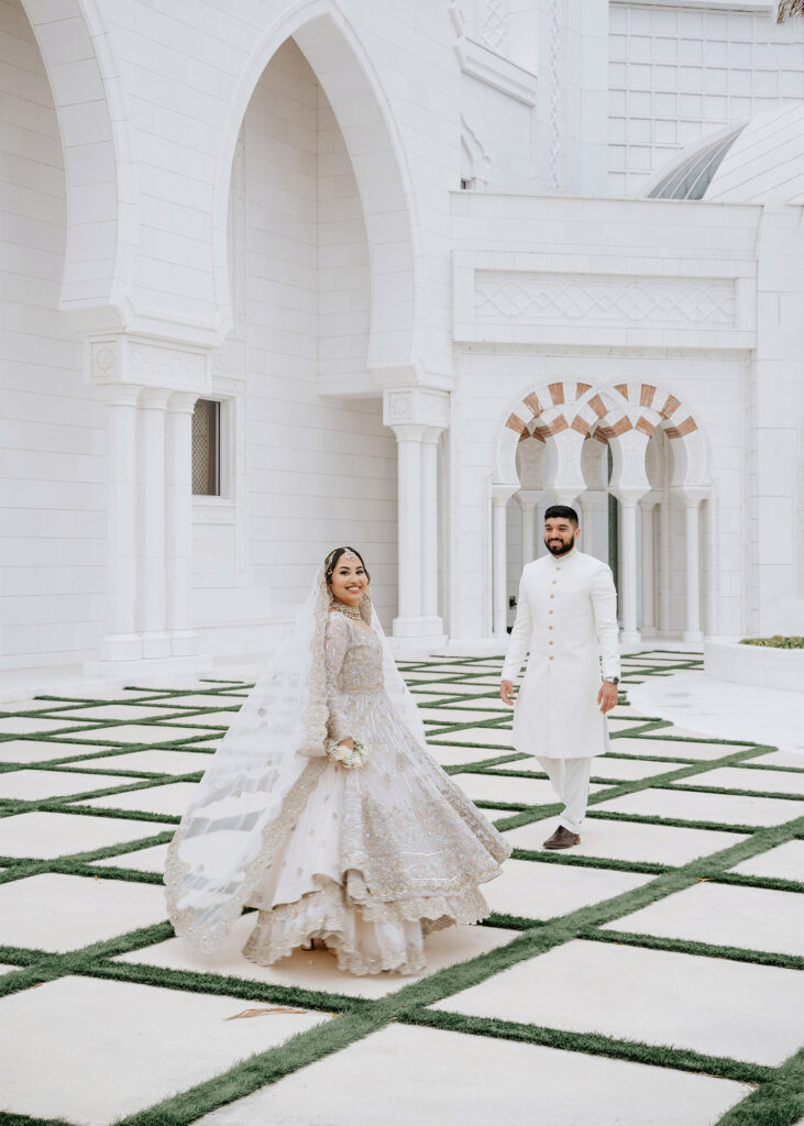 Bride twirling her silver lehenga in the courtyard of Masjid Al-Hayy as the groom in a white sherwani walks toward her, Orlando nikah photographer