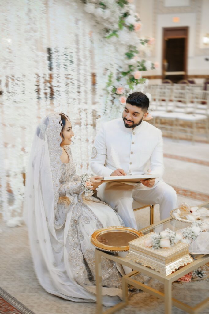 Groom signing the nikah nama with a white feather pen as the bride smiles, nikah at Masjid Al-Hayy, Sanford