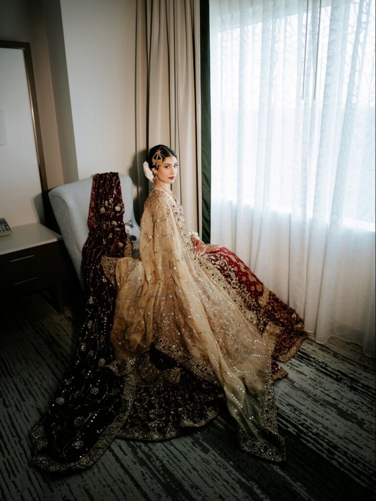 Amen & Shoaib’s Stunning South Asian Wedding at Signia by Hilton & Waldorf Astoria Orlando 17 South Asian bride in a maroon and gold lehenga with a sequined dupatta seated by the window, Orlando shaadi near Disney