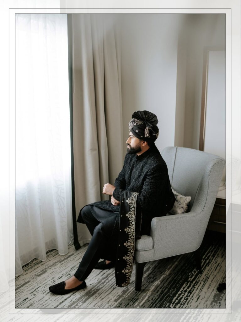Amen & Shoaib’s Stunning South Asian Wedding at Signia by Hilton & Waldorf Astoria Orlando 14 South Asian groom in a black embroidered sherwani and turban sitting by the window on his shaadi day in Orlando
