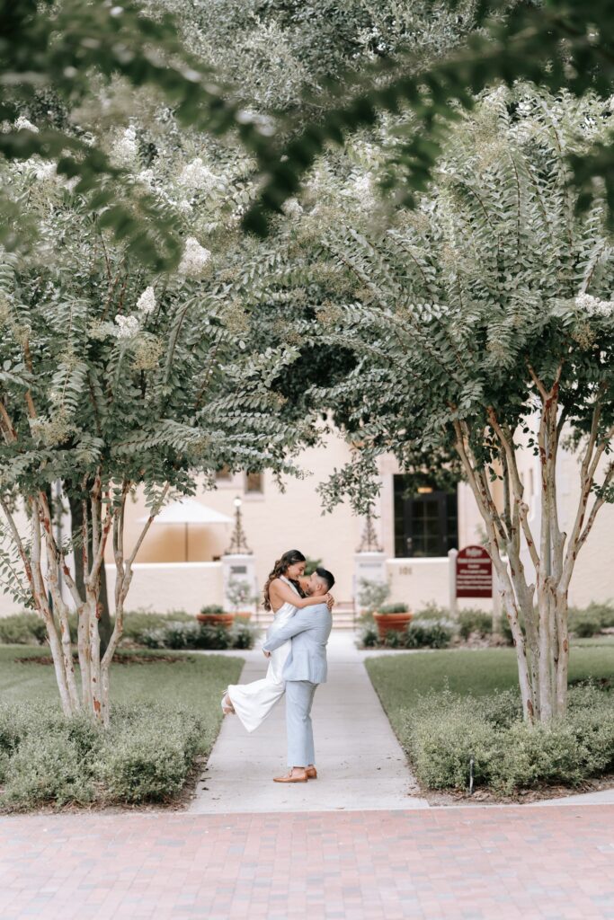 Rollins College engagement photos in Winter Park: couple embracing under white crepe myrtle trees on a campus walkway