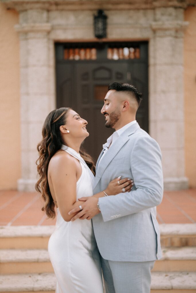 Rahul & Nirali’s Romantic Rollins College Engagement Session 3 Close-up of an engaged couple smiling at each other in front of a carved wooden door, Winter Park engagement photography