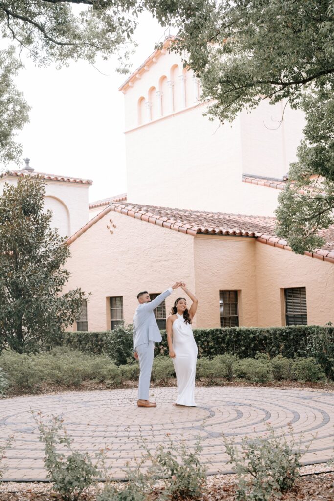 Rahul & Nirali’s Romantic Rollins College Engagement Session 10 Couple twirling on a circular brick labyrinth beside a Mediterranean bell tower in Winter Park