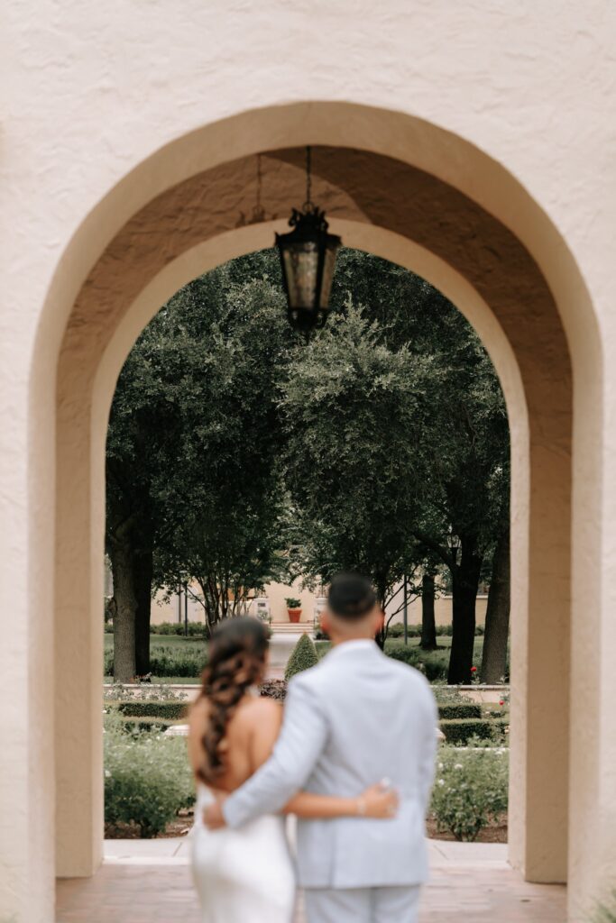 Rahul & Nirali’s Romantic Rollins College Engagement Session 6 Couple framed by a stucco archway with a hanging lantern, looking toward a formal garden