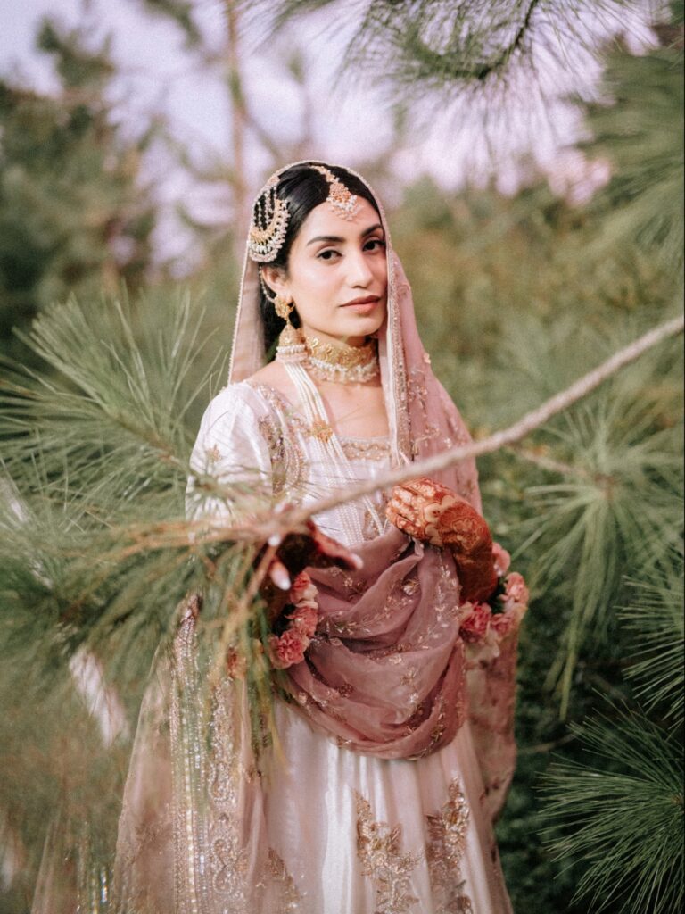 Amen & Shoaib’s Stunning South Asian Wedding at Signia by Hilton & Waldorf Astoria Orlando 13 South Asian bride in an ivory and gold outfit with a blush dupatta among pine branches, Orlando bridal portrait